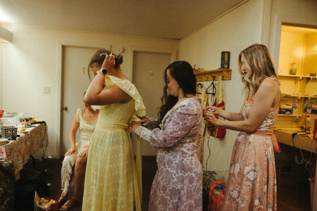 bridesmaids in vintage dresses zipping each other up.