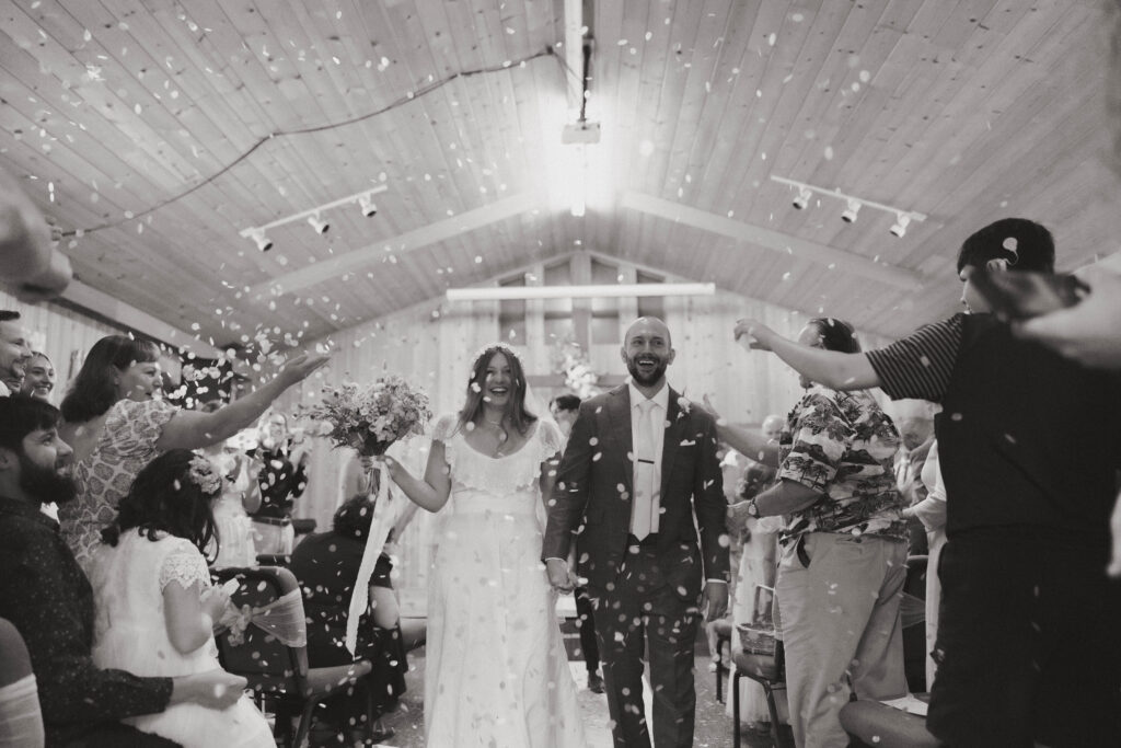 bride and groom walking down the aisle while guests throw confetti.